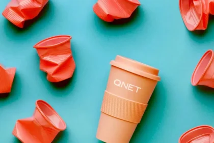 Orange reusable QNET tumbler surrounded by crumpled plastic cups