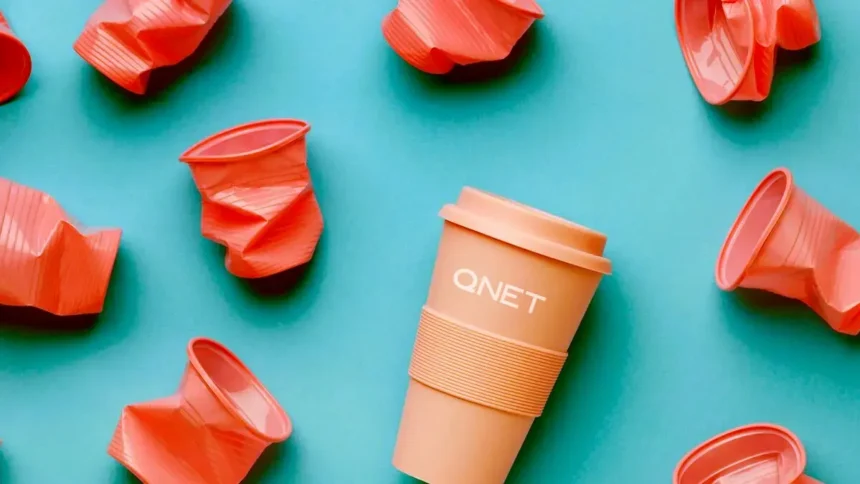 Orange reusable QNET tumbler surrounded by crumpled plastic cups